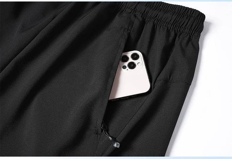 Black pants with a phone peeking out from a pocket on a white background